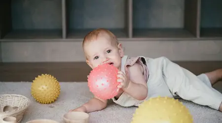 Baby ligt op de grond met bal in hand