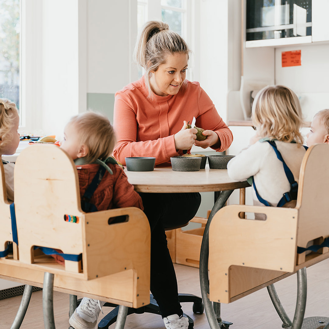 Pedagogisch Medewerker op kinderopvang snijdt fruit voor kinderen aan tafel