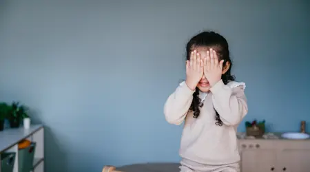 meisje zit op klimrek en houdt haar handen voor haar ogen