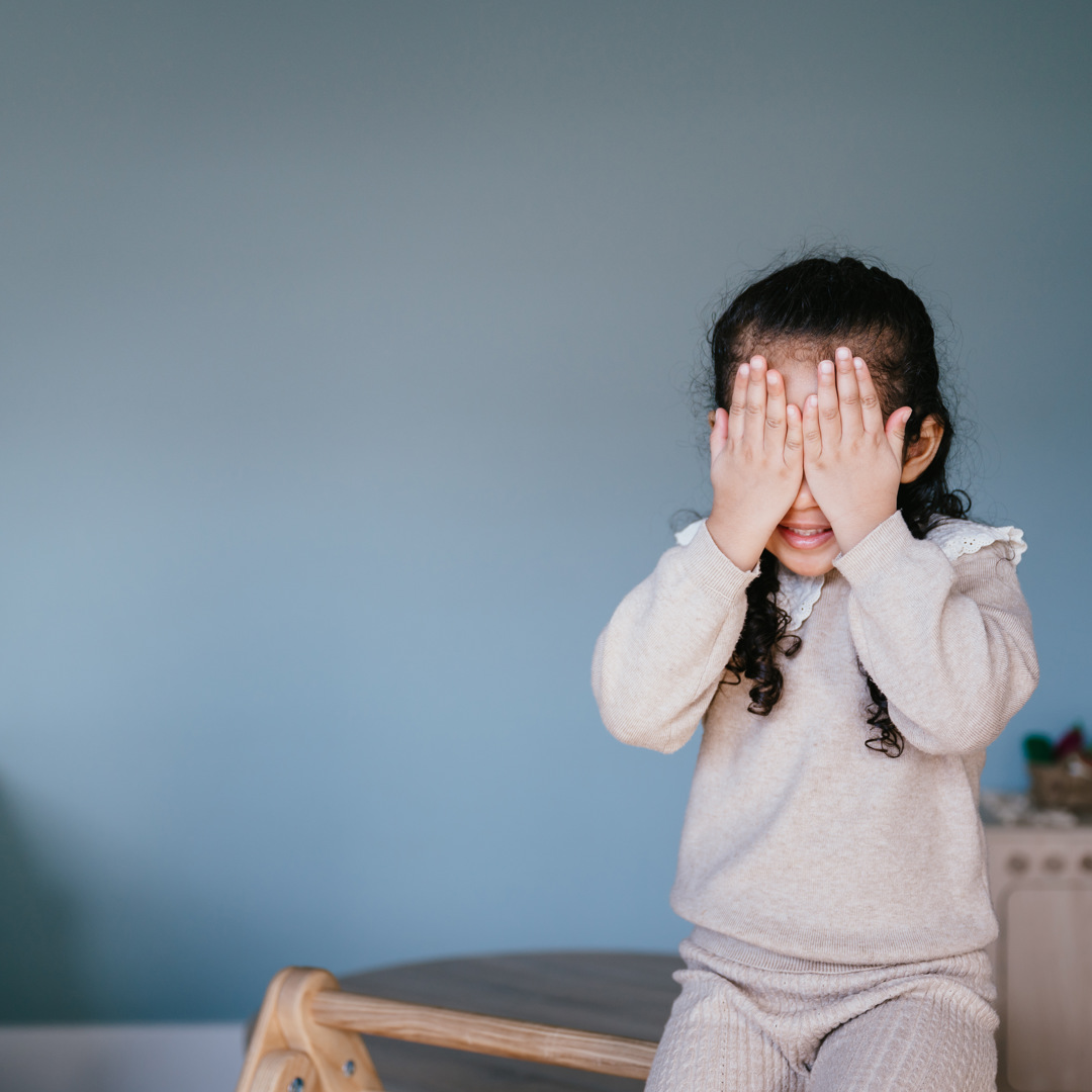 meisje zit op klimrek en houdt haar handen voor haar ogen